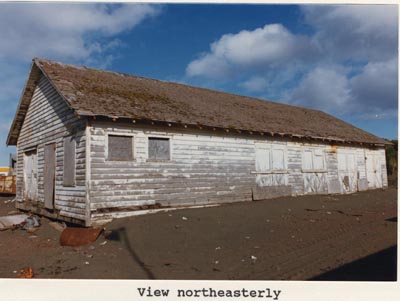 Photo of northeasterly view of the paint shop, a weathered white building.